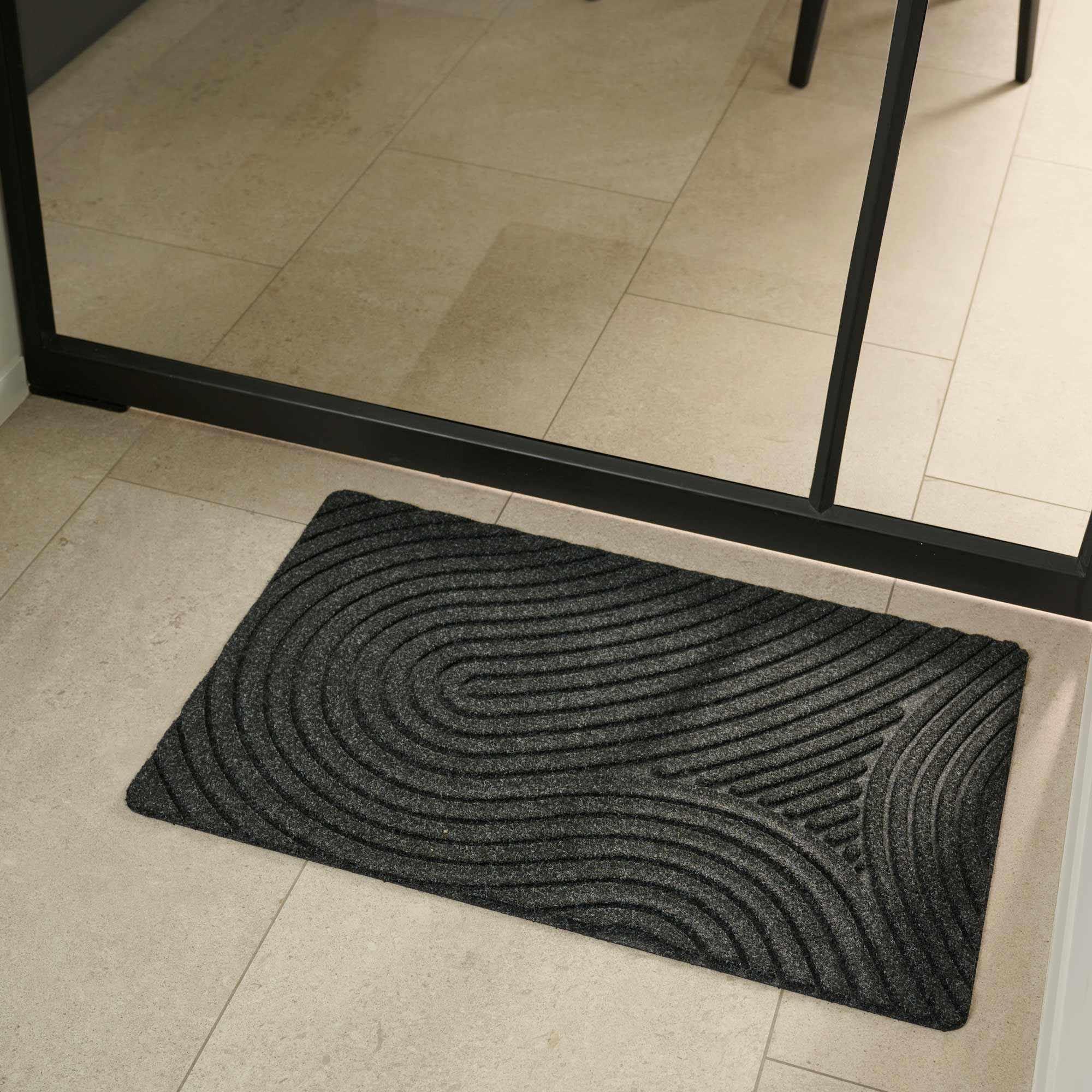 Textured black doormat on a tiled floor with a mirror reflecting the room.