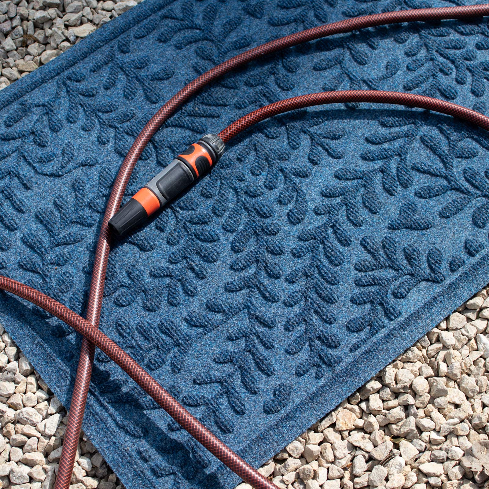 Blue textured mat with a coiled hose on a gravel surface