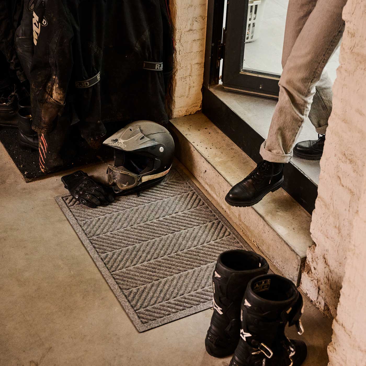 Person getting into a motorcycle garage with gear and boots visible.