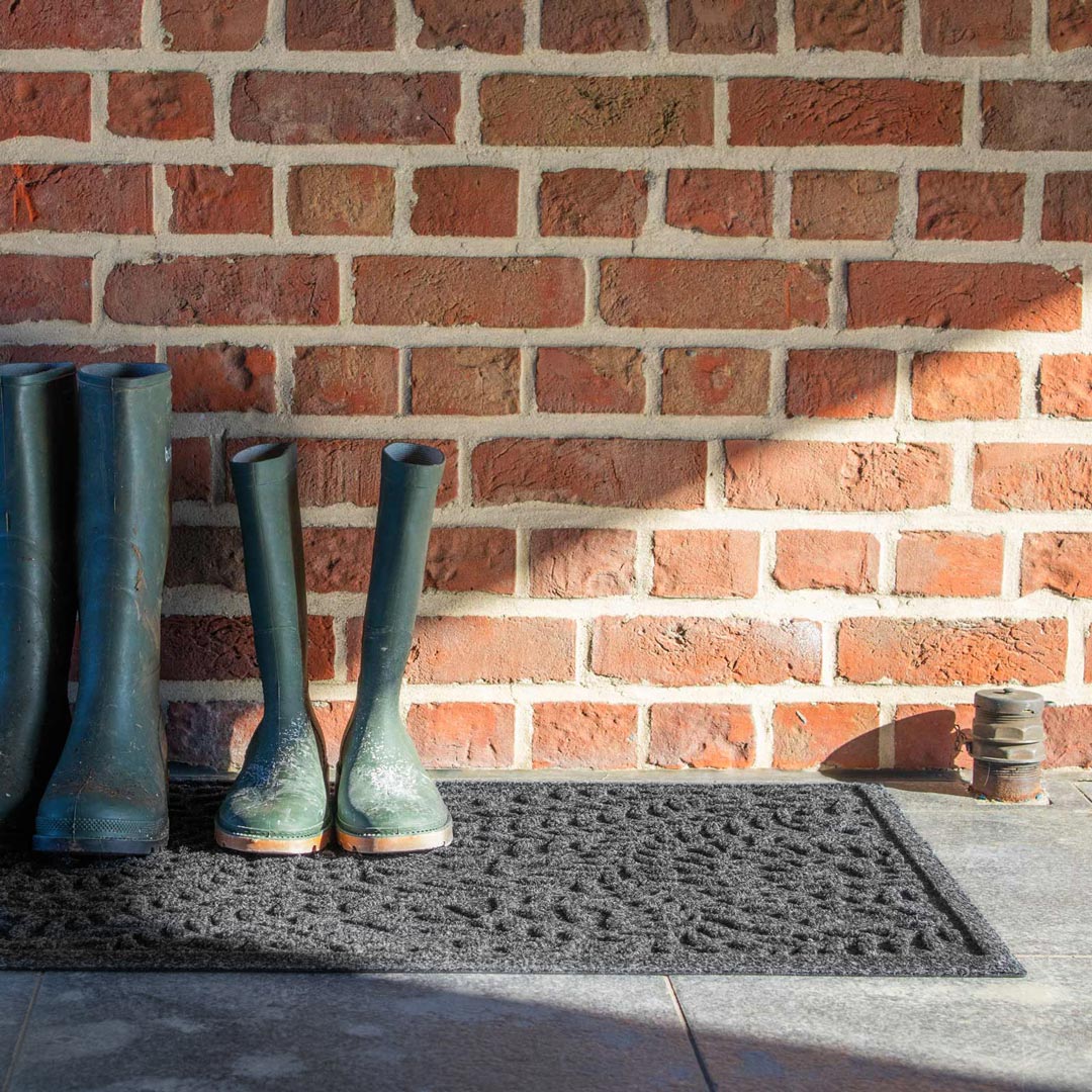 Green boots on a doormat in front of a brick wall
