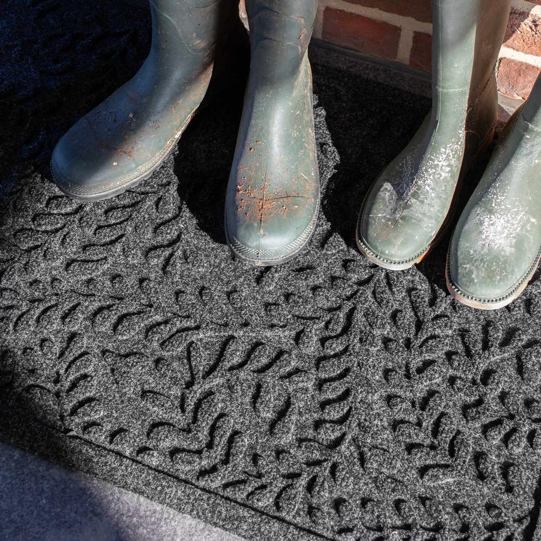 Green rubber boots on a textured mat with a brick wall background