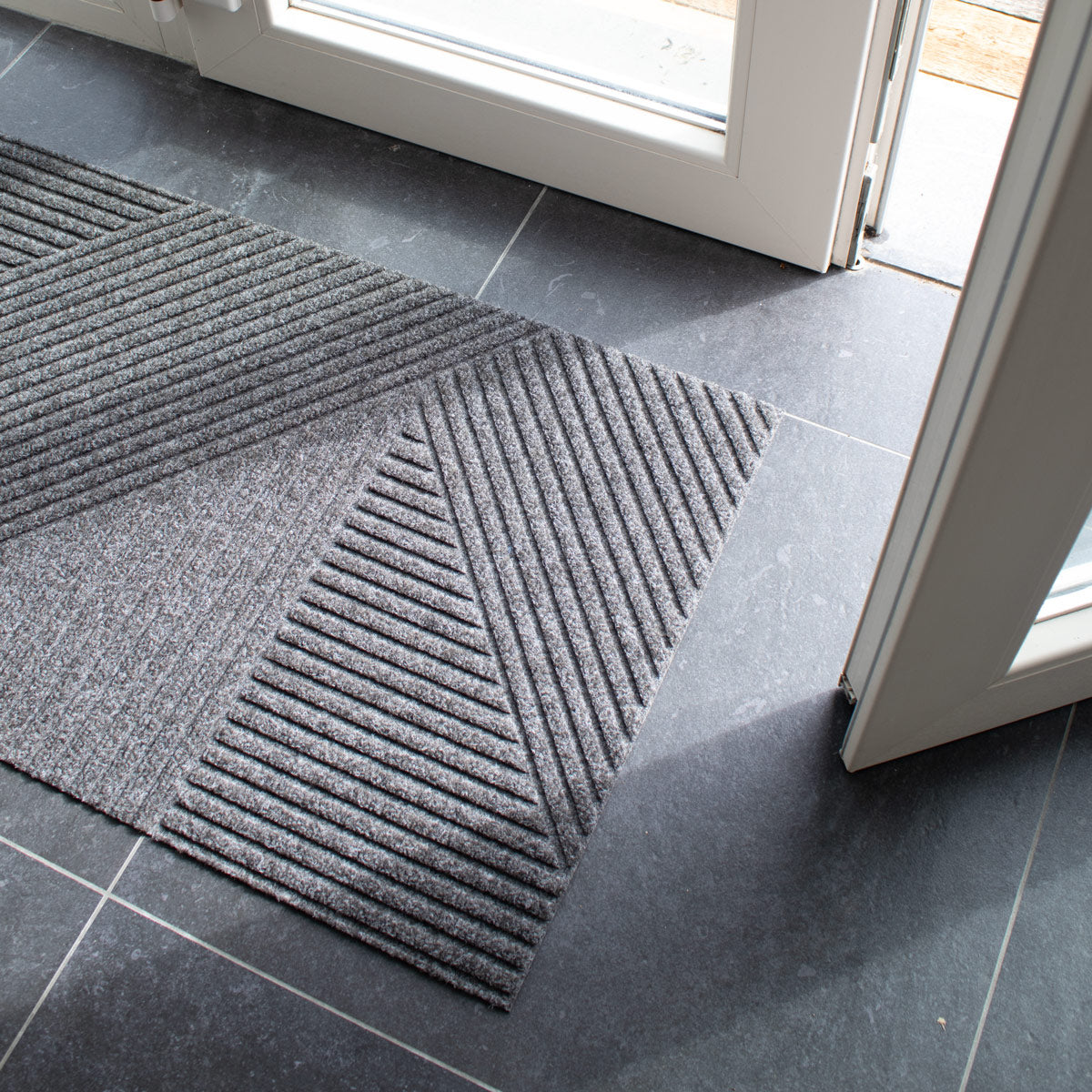 Gray doormat with textured pattern on a tiled floor next to a glass door.