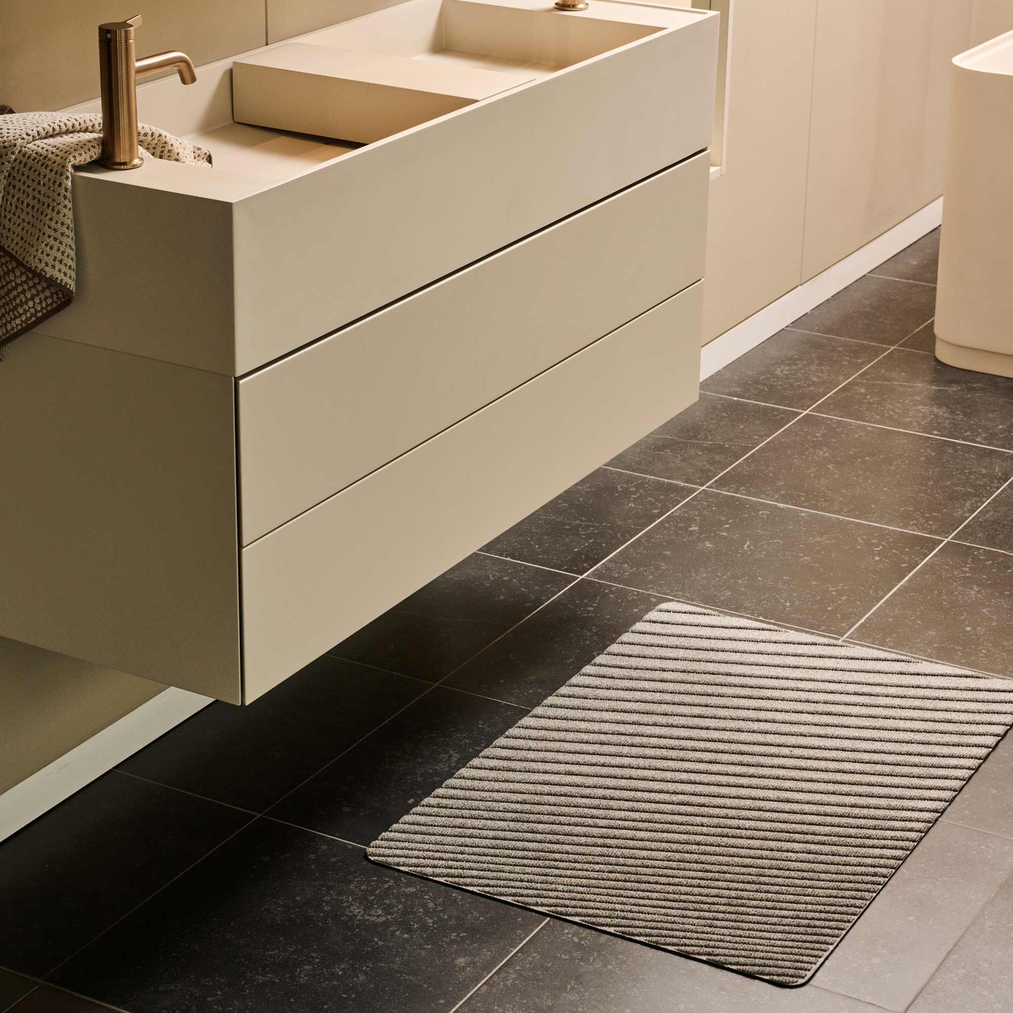 Bathroom with a vanity unit, sink, and textured rug on dark tiled floor.