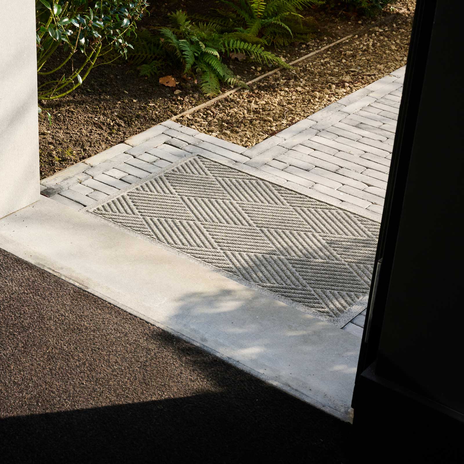 Gray doormat with a diamond pattern on a stone floor.