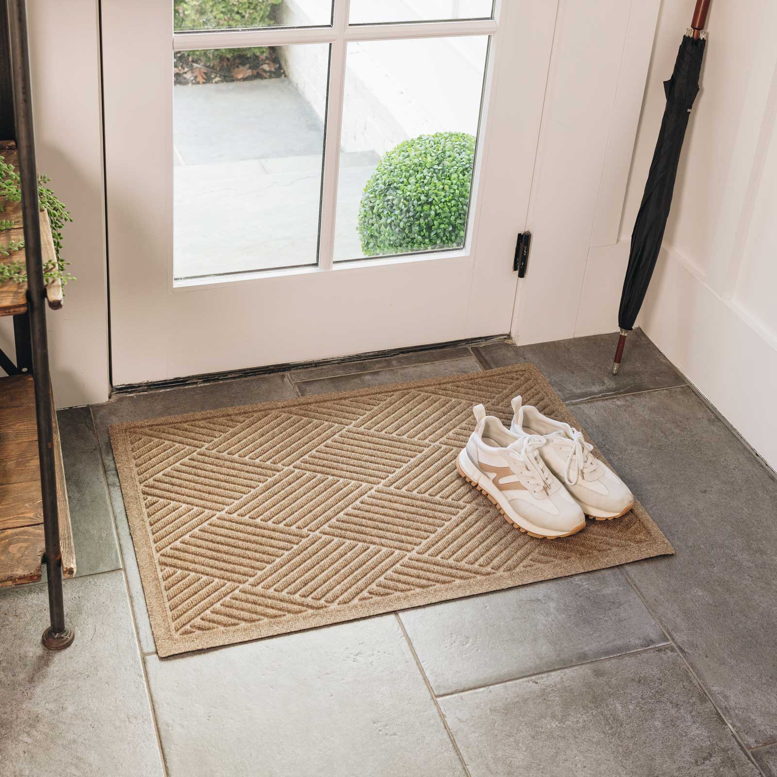 Doormat with shoes on a tiled floor outside a glass door.